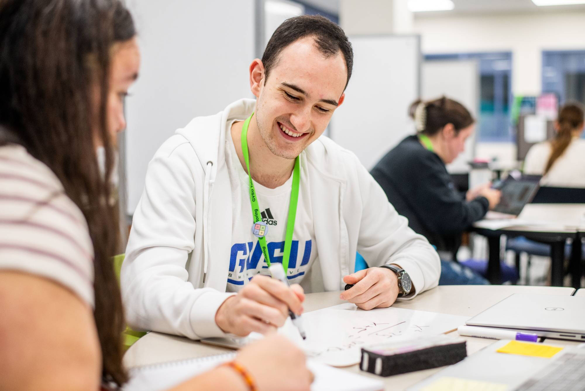 A tutor smiles while helping another student.